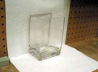  Photo shows two pieces of white paper affixed to a wall and a table top to form a white background for the glass container.