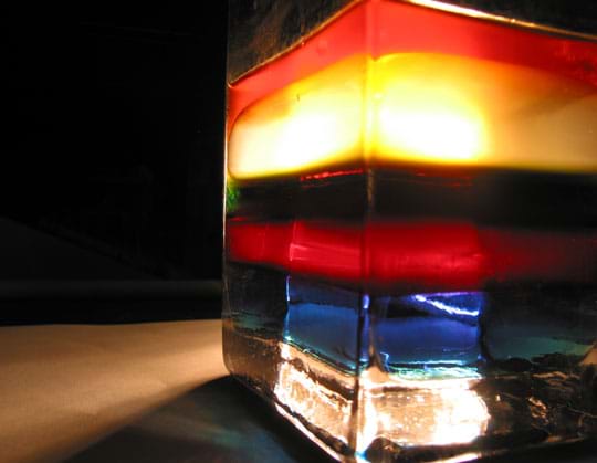 Photo shows layers of blue, red, brown, yellow and orange fluids in a glass container.